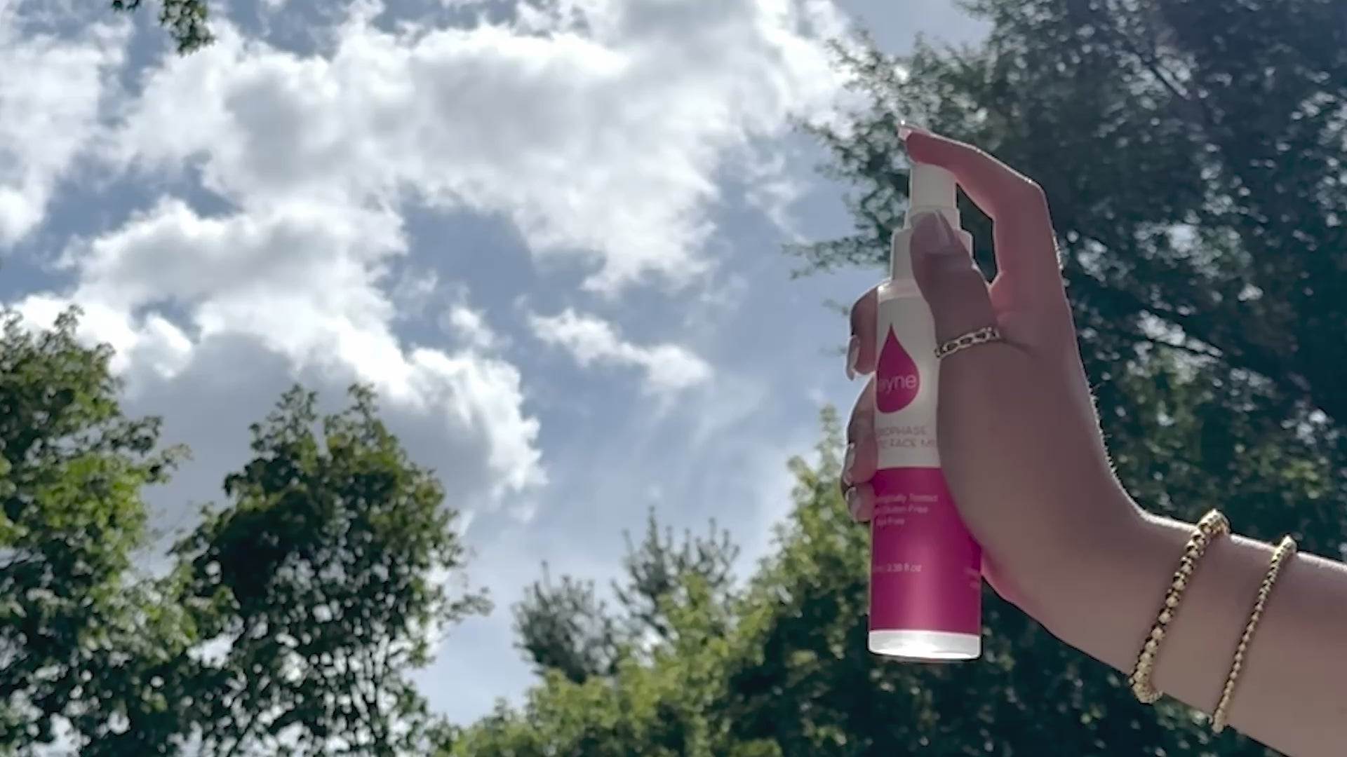 Reiyne HydroPhase Prebiotic Face Mist in a white pump bottle and a pink and white label Spraying into the air with sky and trees